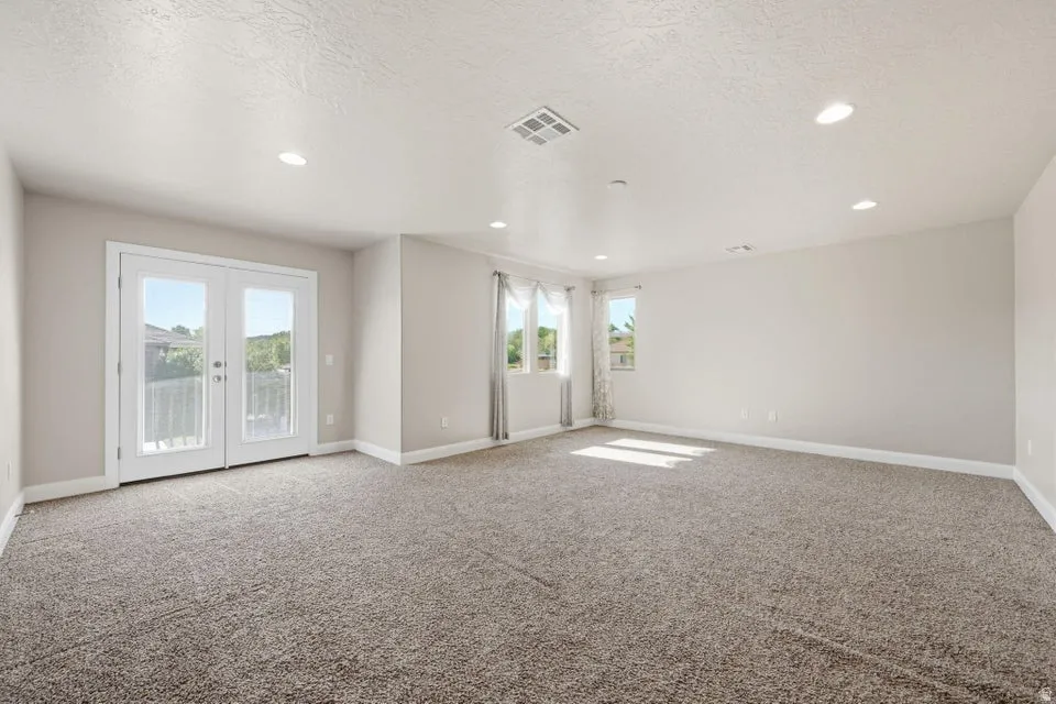 Spacious open room featuring neutral carpet flooring, recessed ceiling lighting, and dual glass sliding doors with transoms that flood the space with natural light