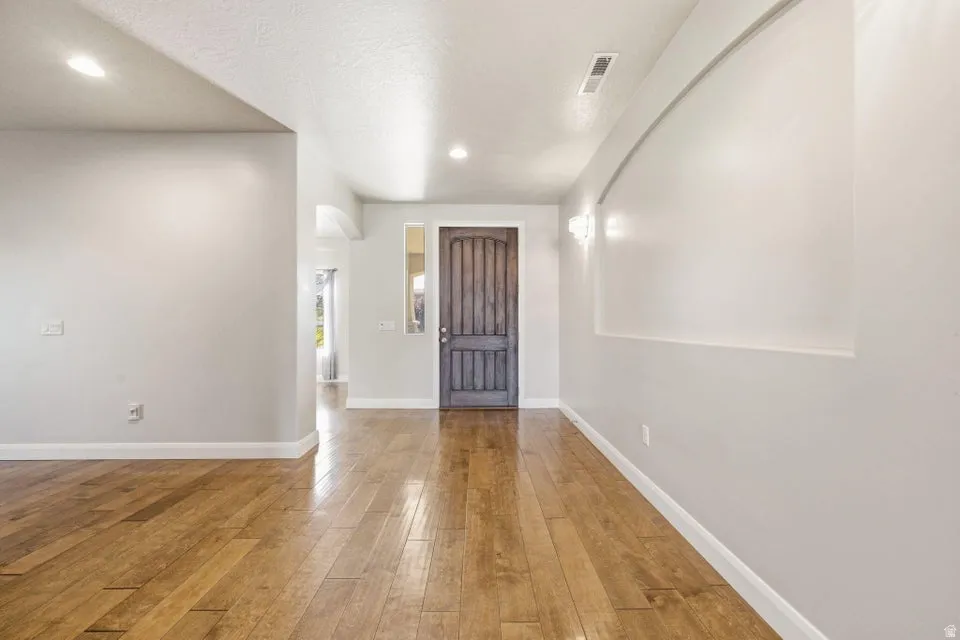 Entryway featuring wood-finish flooring, a substantial wood entry door, and recessed wall paneling with sconce lighting