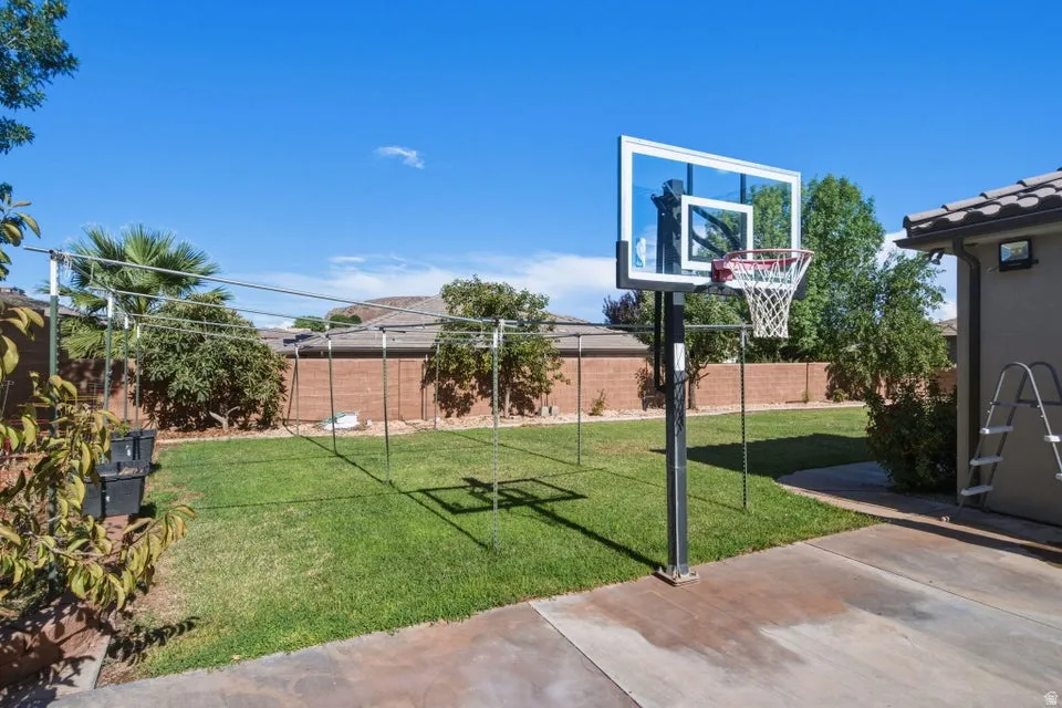 Expansive backyard featuring a concrete patio, a basketball hoop, and a manicured lawn