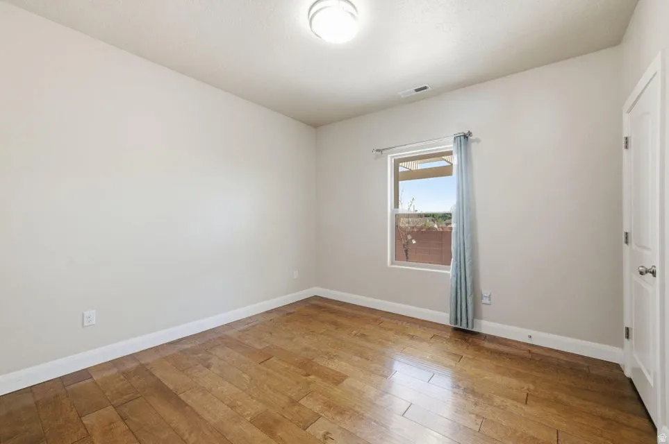 Bright bedroom offering hardwood flooring, generous natural light from large window with custom drapery, and clean white walls