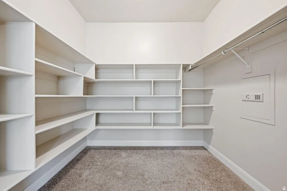 Spacious walk-in closet featuring extensive built-in white shelving and storage solutions throughout, carpeted flooring, and a clothing rod for hanging garments