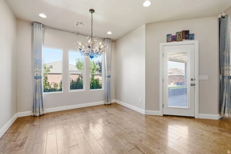 Bright and spacious interior showcasing gleaming wood-finish flooring, soaring ceilings with recessed lighting, and a striking crystal chandelier