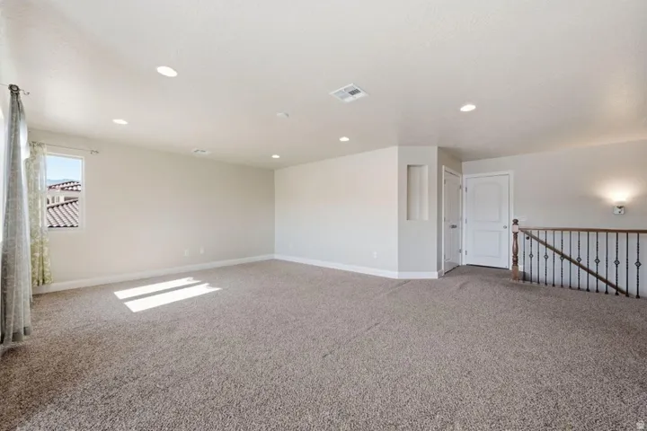 Spacious upper-level bonus room featuring neutral carpet flooring, recessed ceiling lighting, and abundant natural light from a large window