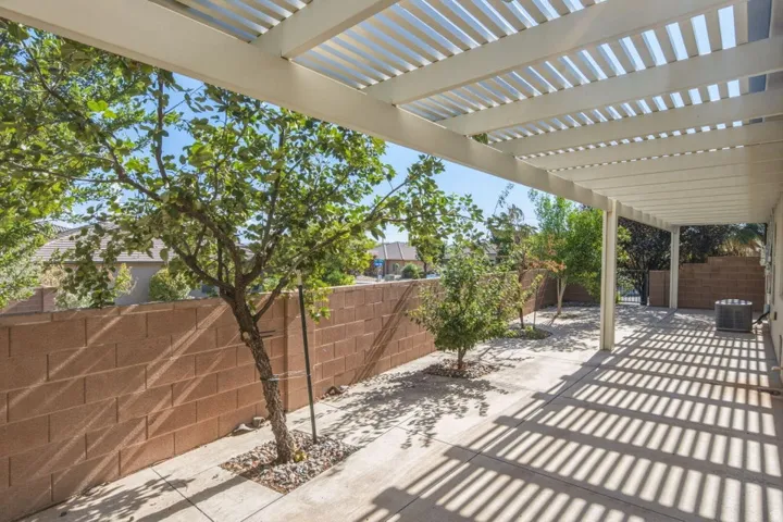 Expansive patio featuring a white slatted pergola, concrete flooring, and a privacy wall