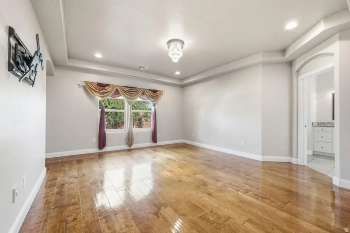 Spacious room featuring wood-finish flooring and a tray ceiling with recessed lighting