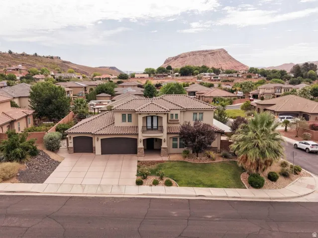 Stucco exterior residence featuring a tile roof, two-car garage, established landscaping, and a second-story balcony