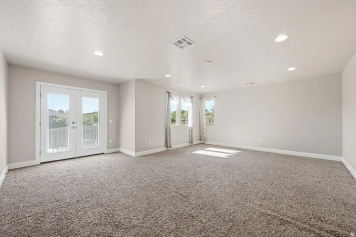 Spacious open room featuring neutral carpet flooring, recessed ceiling lighting, and dual glass sliding doors with transoms that flood the space with natural light