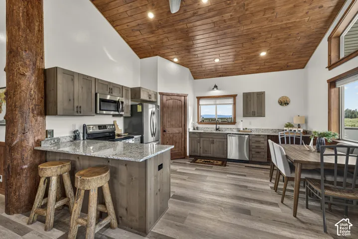 Open-concept kitchen and dining area featuring wood-finish plank ceiling with recessed lighting, stainless steel appliances, granite countertops, and a center island with seating