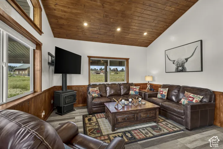 Sophisticated living room showcasing rich leather seating, a wood-burning stove with black metal surround, and warm wood-finish ceiling with recessed lighting