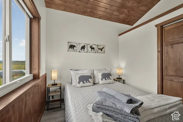 Serene bedroom retreat featuring warm wood ceiling beams and trim, abundant natural light from large windows, wood-finish flooring, and tasteful décor including animal artwork