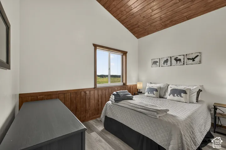 Charming bedroom featuring wood-paneled walling detail, vaulted wood-finish ceiling, and a picture window framing pastoral scenery