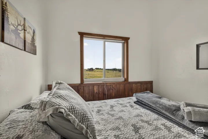 Bedroom featuring a window with natural wood trim, wood-paneled wainscoting, and white painted walls