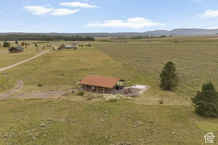 Expansive open land with a residential structure featuring a red metal roof and an outdoor patio area