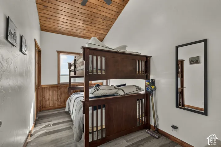 Room featuring wood-finish flooring, white walls with an accent of wood paneling, and a vaulted wood-plank ceiling