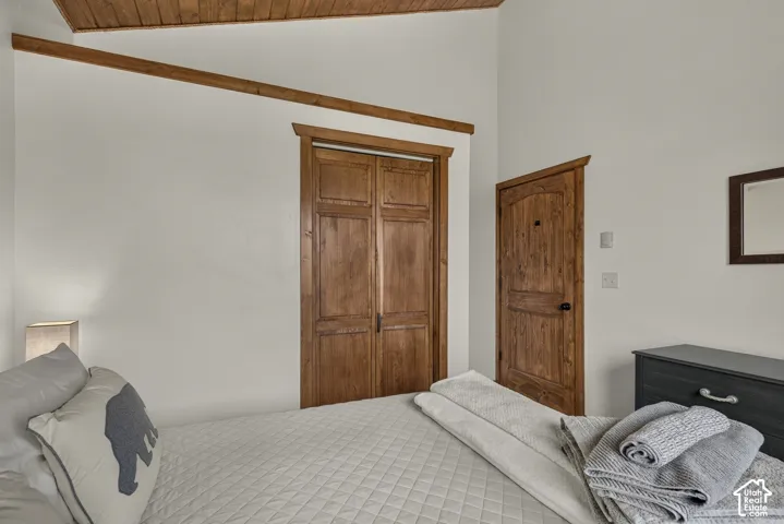 Spacious bedroom showcasing exposed beam ceiling detail, wood-finish double doors with traditional paneling, hardwood entry door, and neutral wall finishes