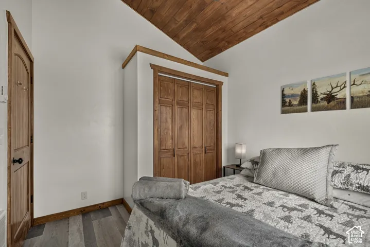 Bedroom featuring vaulted wood-finish ceiling, wood-frame wardrobe with four-panel doors, wood-finish flooring, and coordinated bedding with decorative pillows