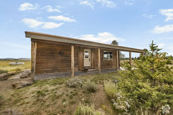 Rustic wood-sided cabin with covered front porch, featuring large windows and an open-air covered entry