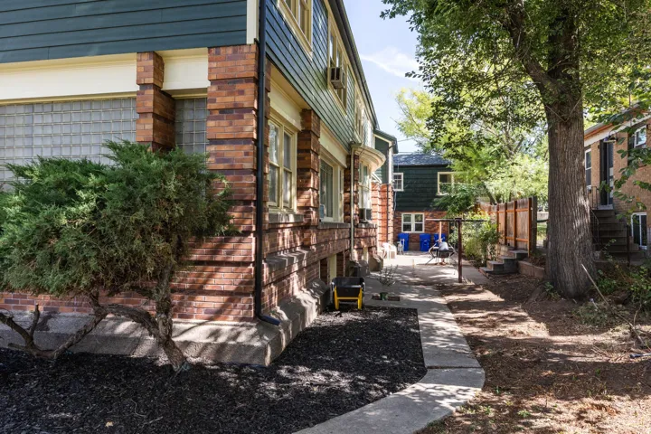 Brick and siding exterior featuring glass block windows, mature perimeter landscaping, a concrete pathway, and a large shade tree