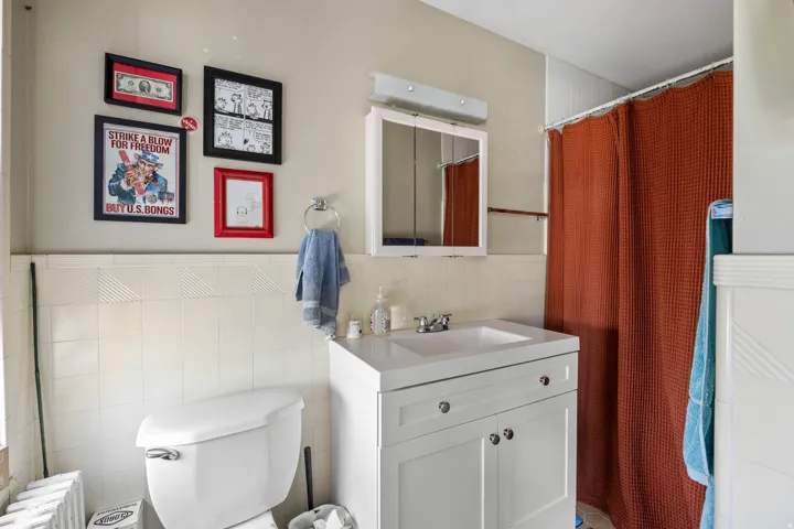 Bathroom featuring a white vanity with integrated sink, a mirrored medicine cabinet, and white tiled walls