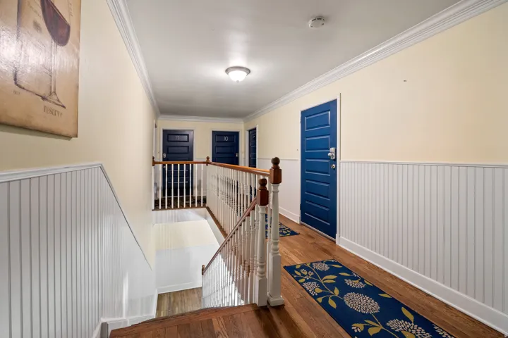 Staircase and hallway featuring wood-finish flooring, white beadboard wainscoting, and crown molding