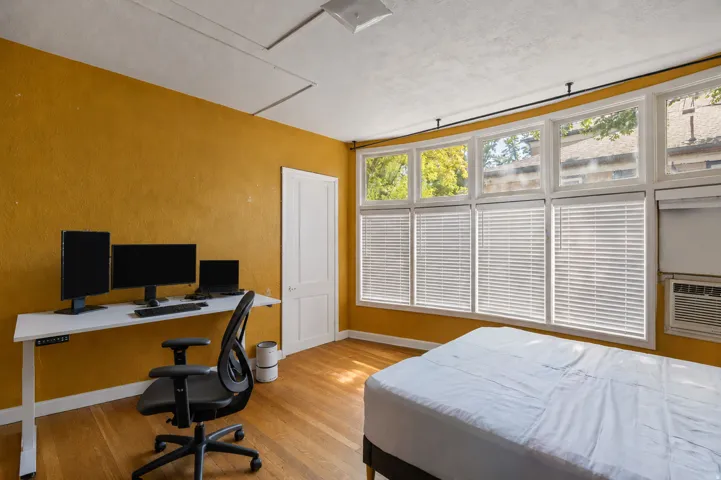 Room featuring multiple windows with blinds, wood-finish flooring, and a white paneled door