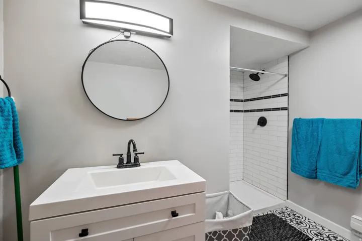 Bathroom featuring a white vanity with integrated sink, black-finish faucet, round black-framed mirror, and an overhead vanity light