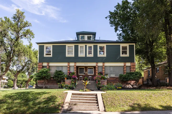 Multi-level residence featuring a dark green siding facade and a brick foundation with column details