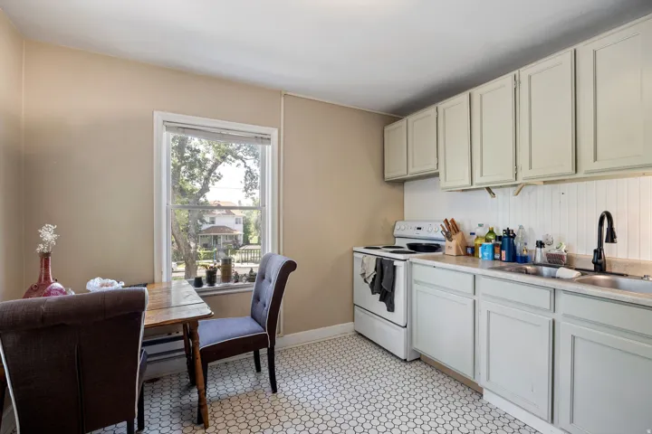 Kitchen featuring white appliances, a black matte gooseneck faucet, light-colored cabinetry, and white hex tile flooring