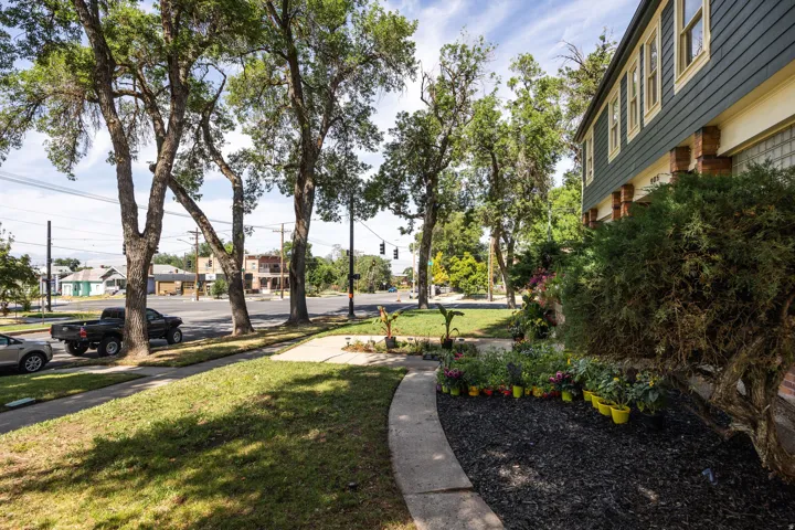 Front exterior with dark green horizontal siding, exposed brick columns, and a landscaped garden bed with dark mulch