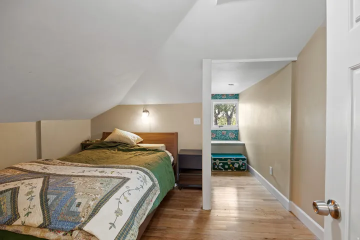 Sloped ceiling bedroom featuring hardwood flooring, a wall-mounted light fixture, and a recessed window nook with built-in shelving