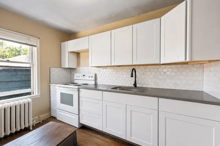 Kitchen featuring bright white cabinetry, a white tile hexagon backsplash, dark countertops, a black gooseneck faucet, and stainless steel appliances