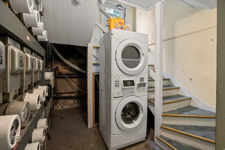Laundry area featuring a stackable washer and dryer unit, utility meters, and a functional staircase