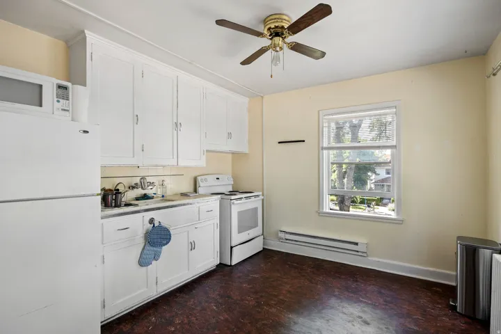 Kitchen space featuring white cabinetry, a single window with blinds, and wood-finish flooring