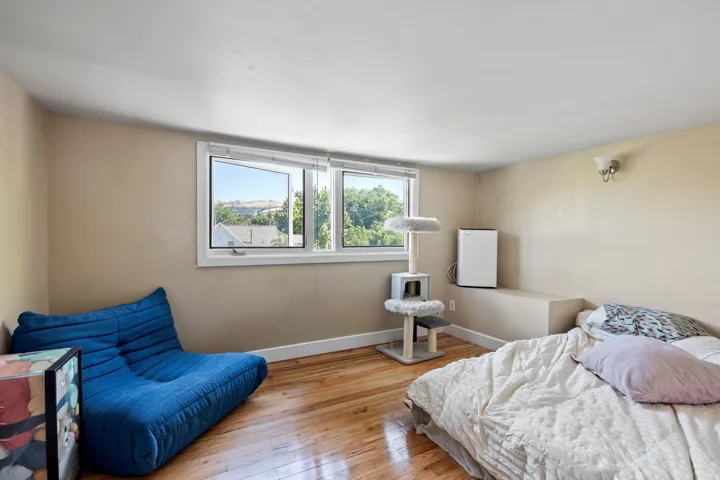 Hardwood flooring throughout this room, featuring multiple windows, a neutral wall color, white trim, and a wall-mounted light fixture