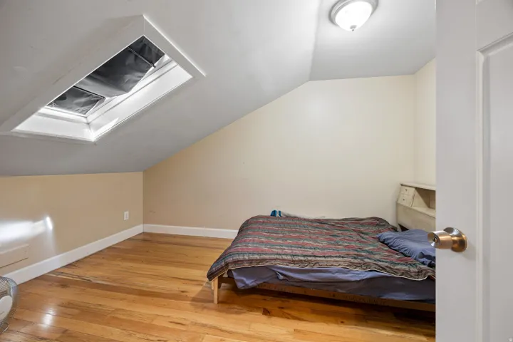 Attic room featuring a skylight with integrated shade, wood-finish flooring, painted walls, and white trim