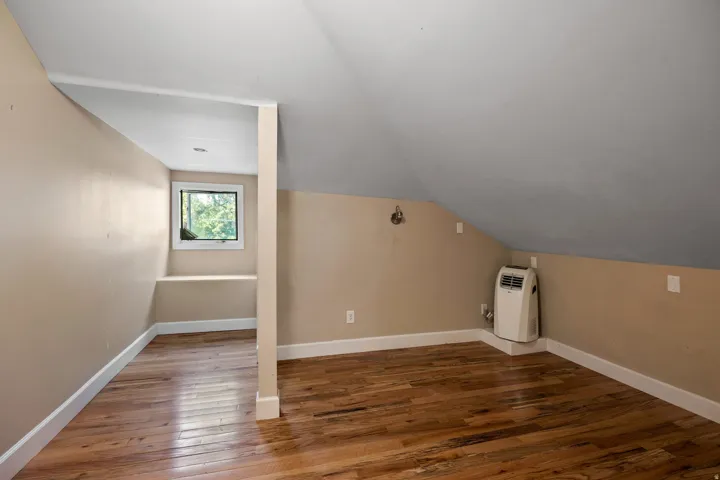 Interior space featuring sloped ceilings, wood-finish flooring, neutral-toned walls, and a recessed window