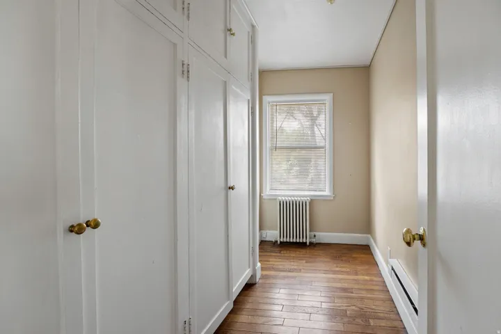 Built-in white cabinetry with brass hardware, wood-finish flooring, a single window with blinds, and light-toned walls