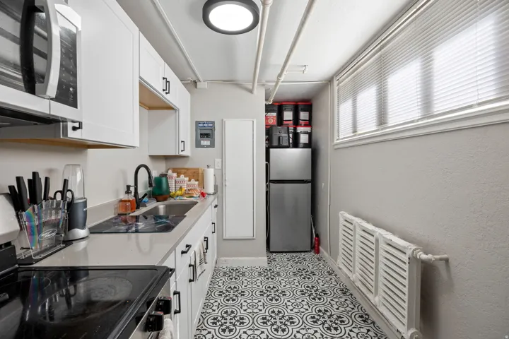 Compact kitchen featuring white cabinetry with black hardware, a stainless steel over-the-range microwave, solid surface countertops, and patterned floor tiles