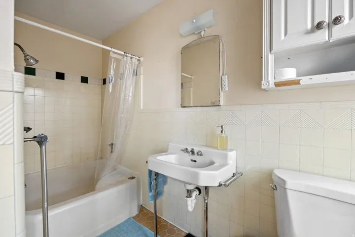 Bathroom featuring a pedestal sink, white tile wainscoting, and a built-in medicine cabinet