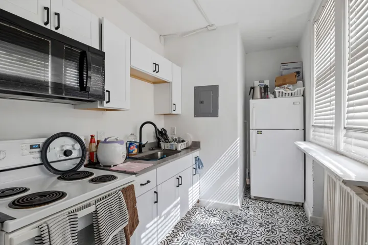 Galley kitchen featuring white cabinetry with matte black hardware, a stainless steel sink with a matte black faucet, durable countertops, and patterned floor tile