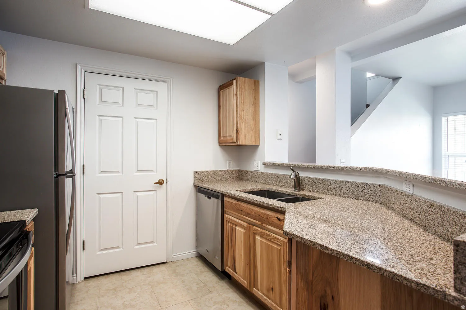 Modern kitchen featuring rich wood cabinetry with ample storage, expansive granite countertops with extended bar seating, stainless steel appliances including a built-in refrigerator, and recessed ceiling lighting