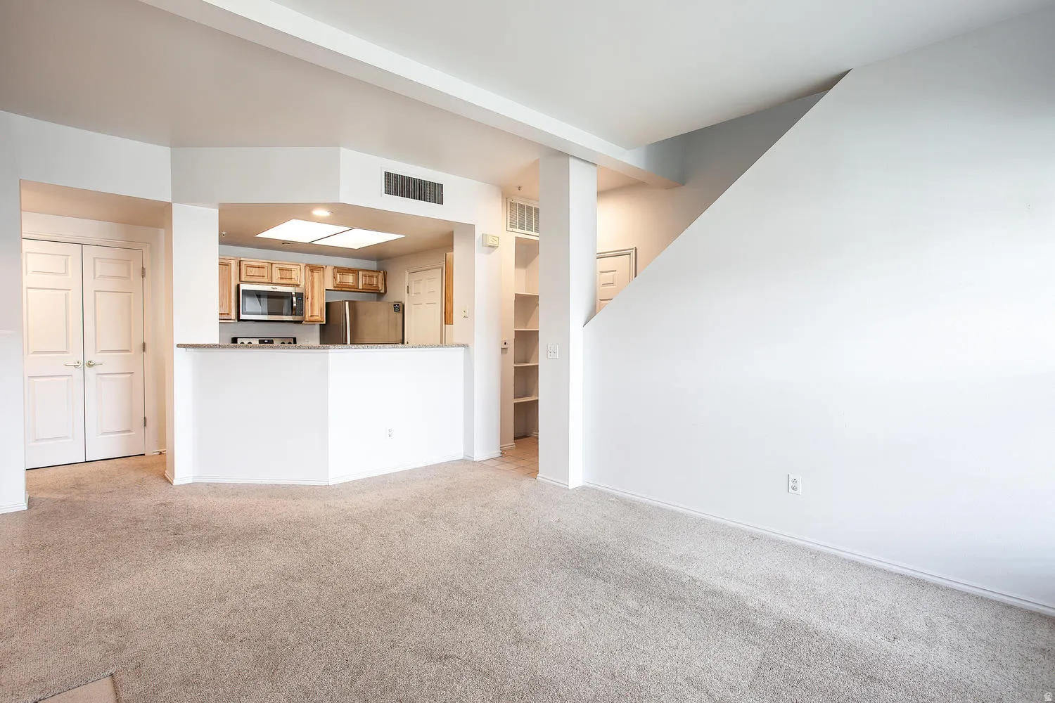 Open-concept living space featuring a curved white kitchen island with wood-finish cabinetry, stainless steel appliances, and ample counter workspace