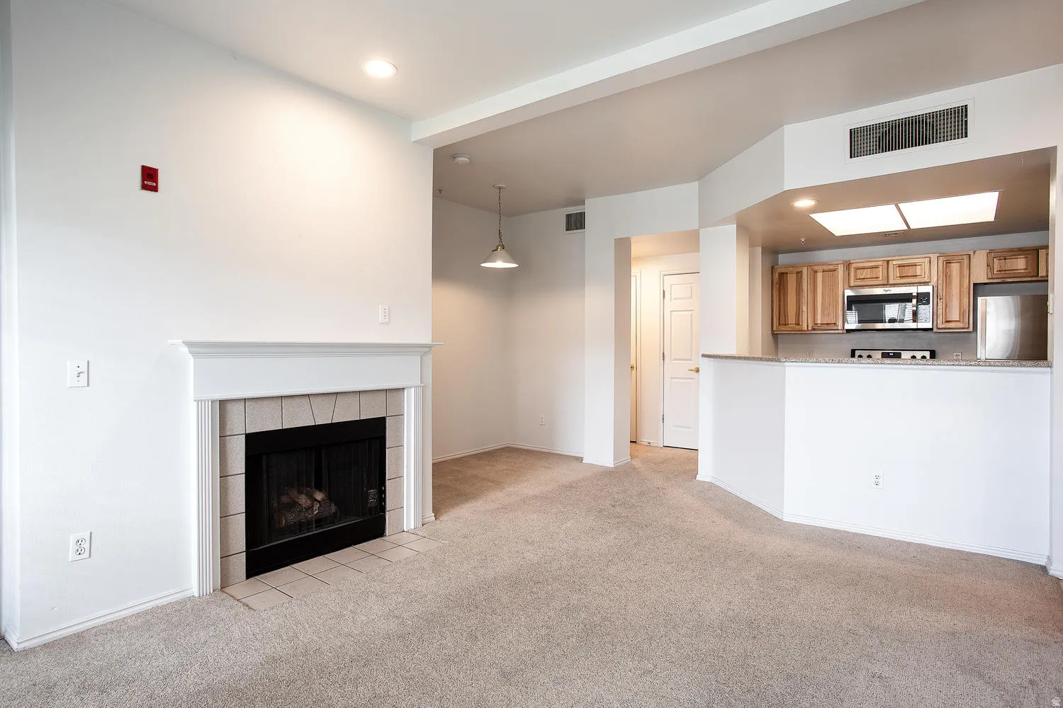 Open-concept living area featuring a wood-burning fireplace with tile surround and white mantel, neutral carpet flooring, recessed lighting, and pendant fixture