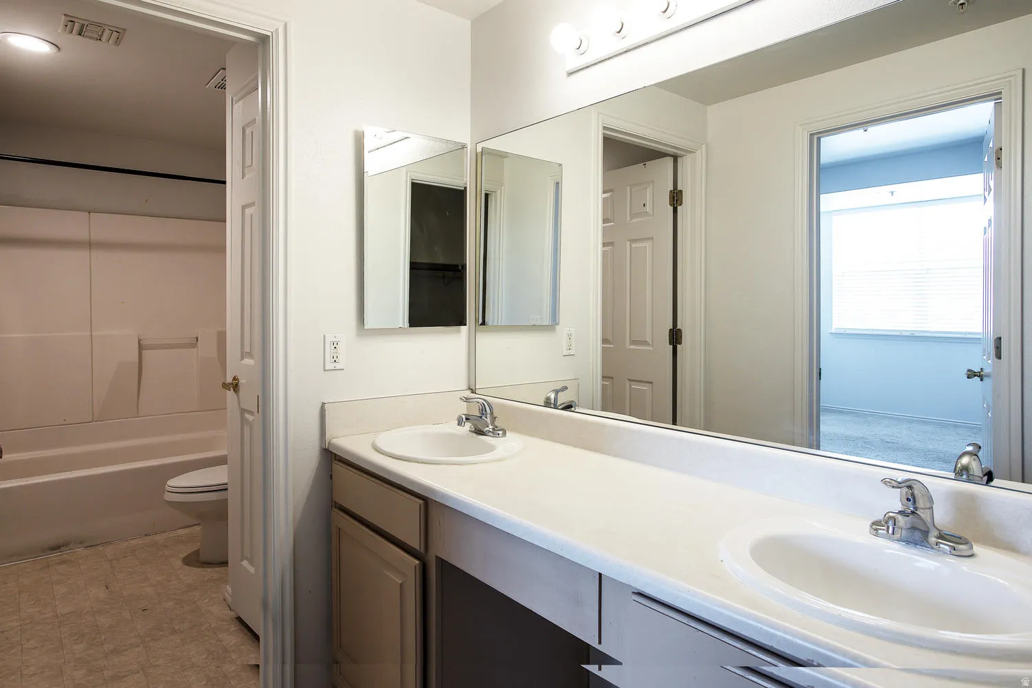 Dual-sink vanity featuring white porcelain basins, wood-finish cabinetry, and a continuous countertop with chrome faucet fixtures
