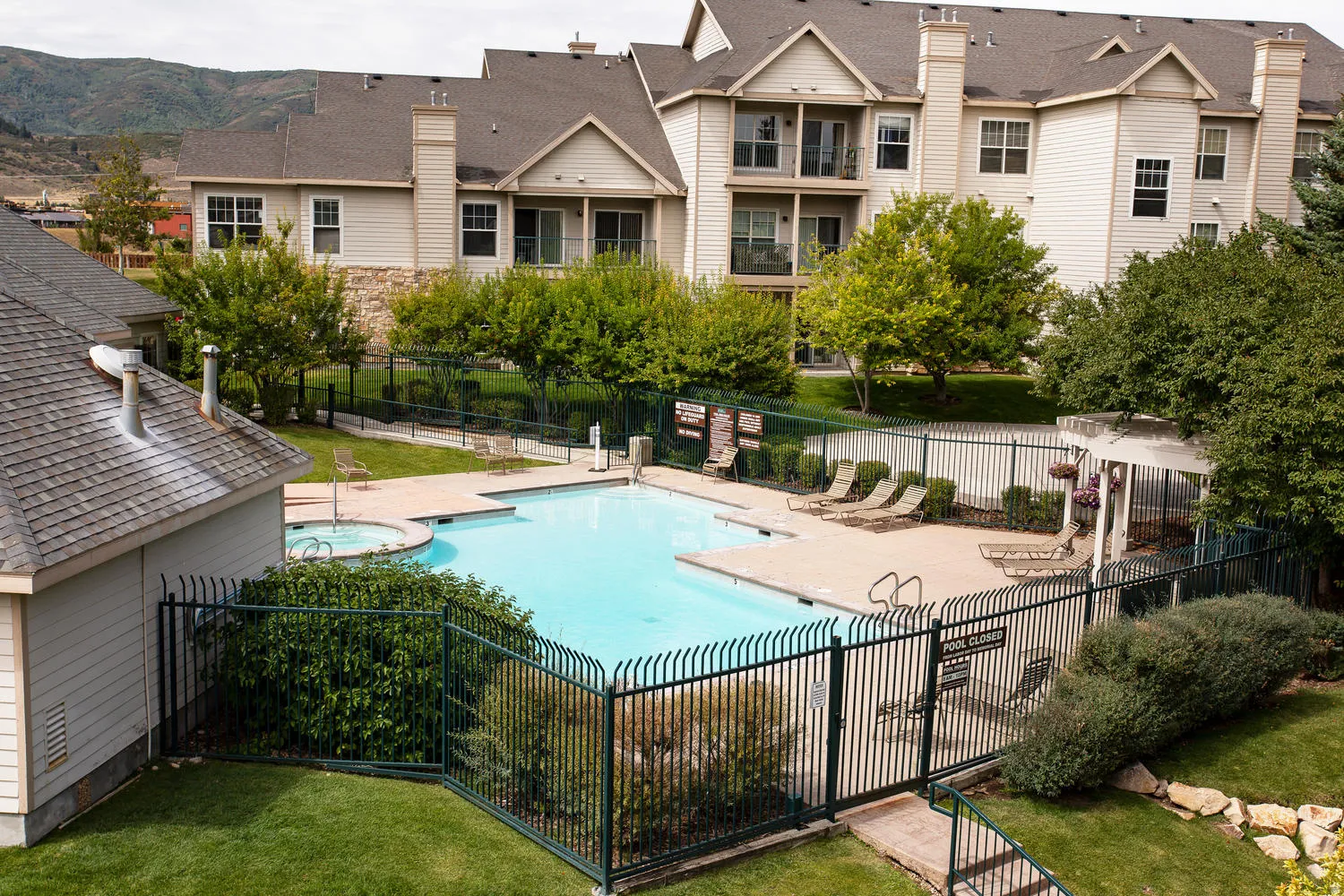 Resort-style community pool featuring crystal-clear waters, surrounded by black metal fencing and mature landscaping
