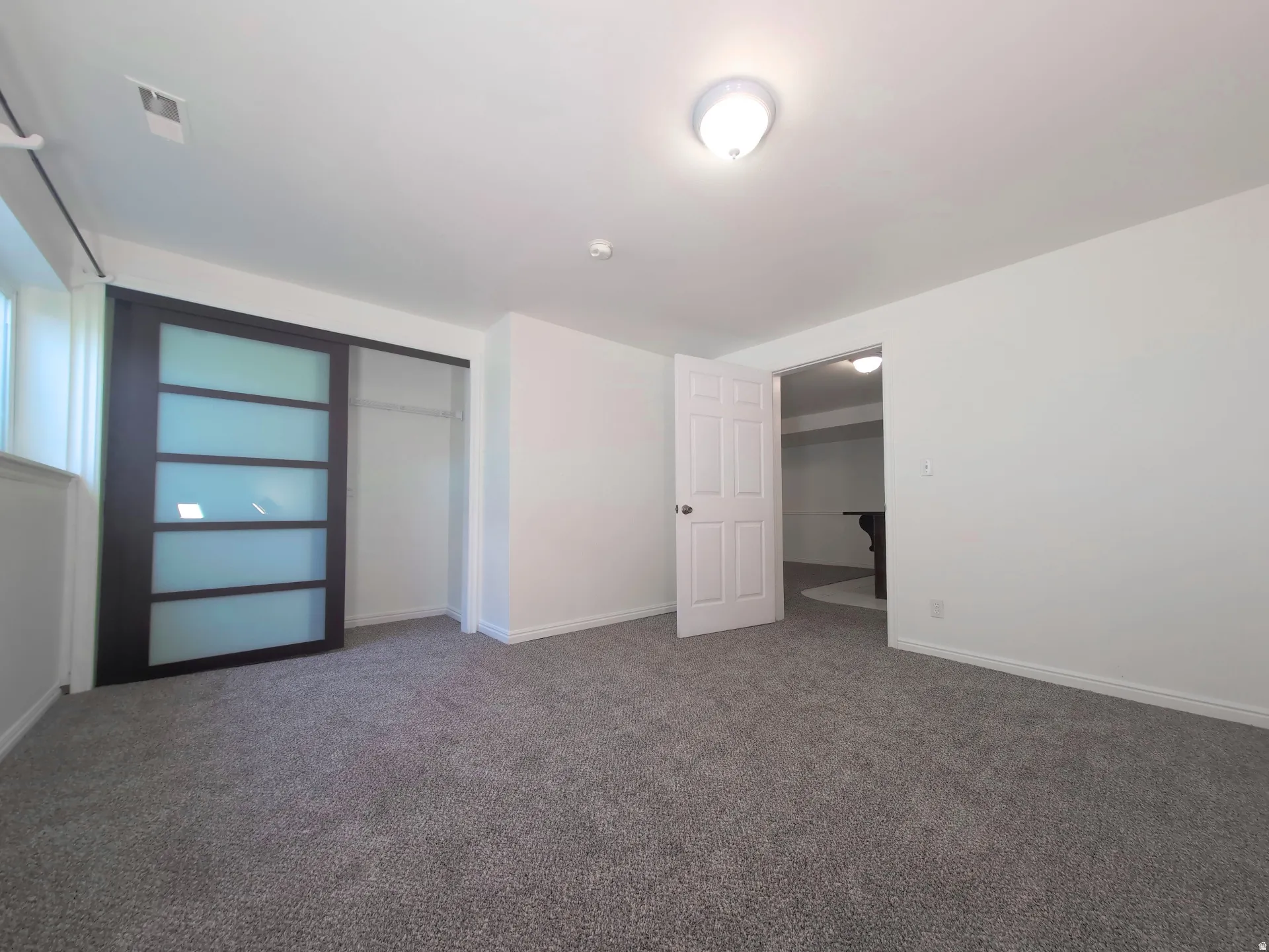 Spacious room featuring gray carpet flooring, white walls, and a contemporary sliding closet door with frosted panels
