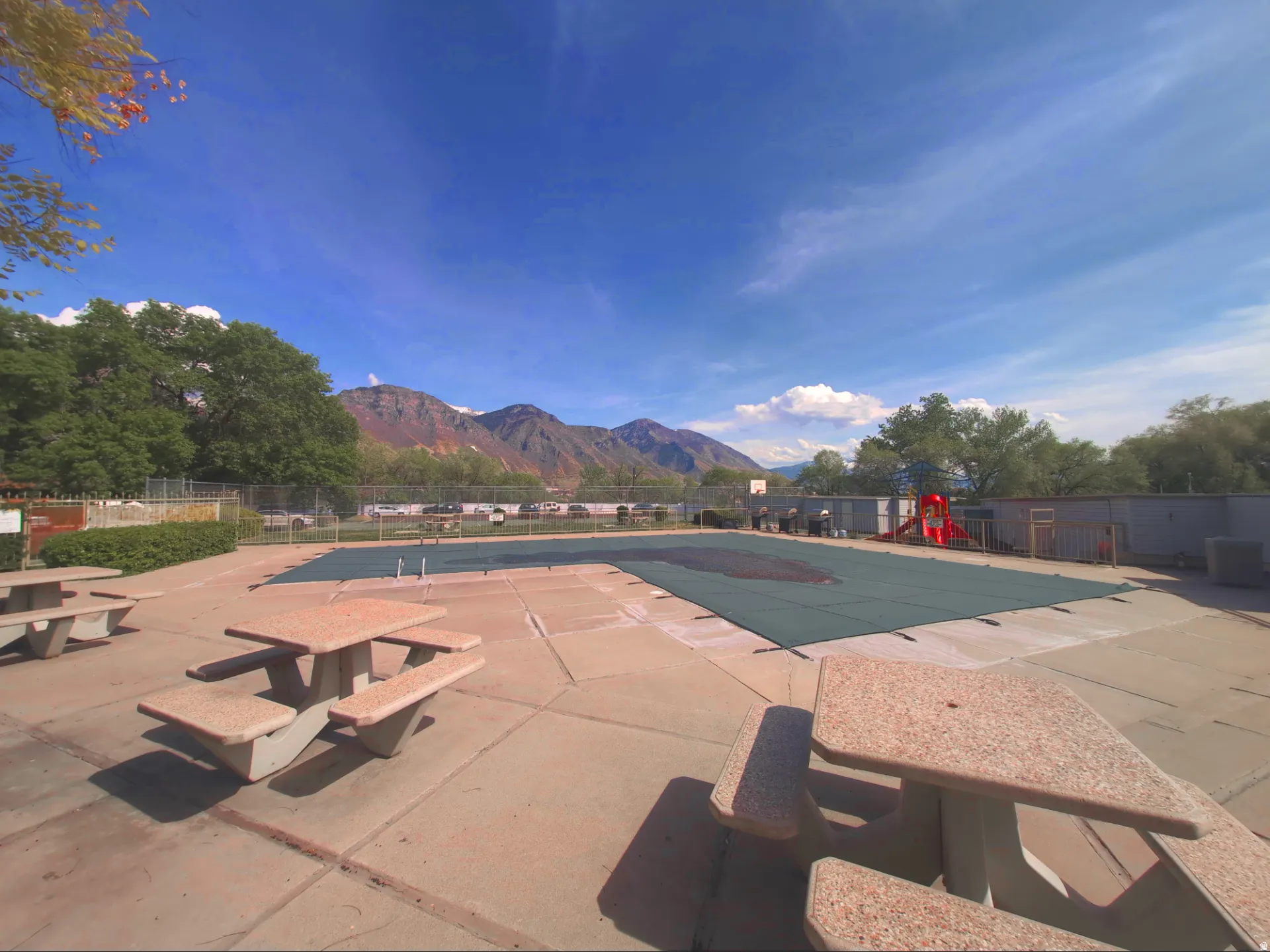 Outdoor swimming pool area with concrete patio, multiple picnic tables, and mountain backdrop