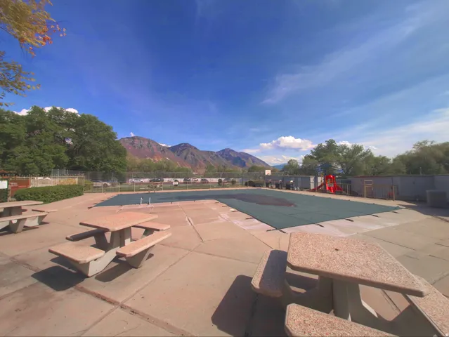 Outdoor swimming pool area with concrete patio, multiple picnic tables, and mountain backdrop