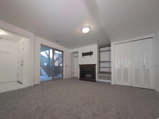 Spacious lower-level recreation room featuring neutral carpeting, a gas fireplace with surround, and abundant natural light from glass doors opening to exterior stairs