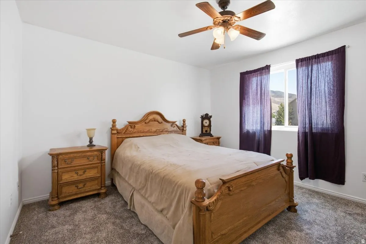 Bedroom featuring a window with purple drapes, a ceiling fan with integrated lighting, and neutral-toned carpeting